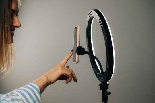 Woman touching smartphone on ring light stand for video recordin