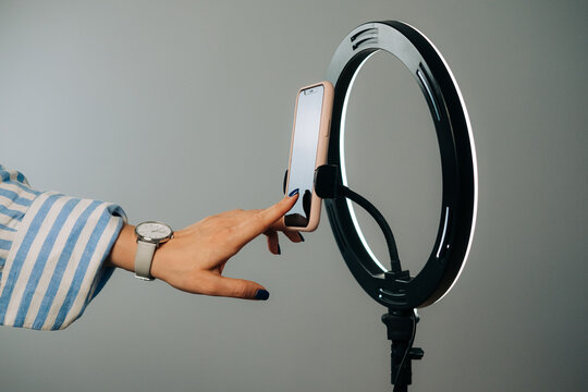 Female hand adjusting smartphone on ring light for video content