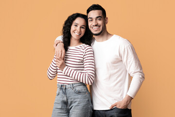 Portrait of happy embracing middle eastern couple posing over yellow studio background, cheerful young arab man and woman looking and smiling at camera, enjoying time together, copy space