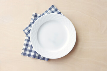 Empty white plate with blue fabric napkin on wooden table. Top view.	