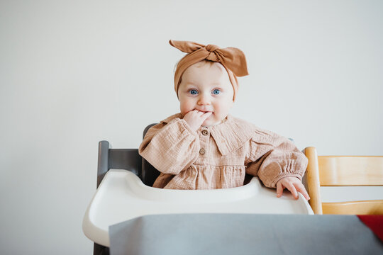 baby girl with big blue eyes sits in highchair looking around.