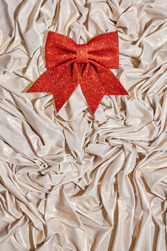 Small red glitter bow placed on a shiny fabric base