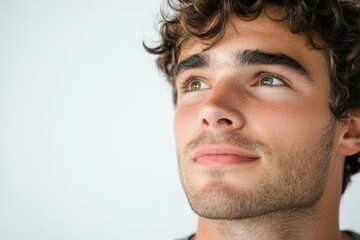 Fototapeta premium Young handsome man with a dreamy and cheerful expression, close-up portrait against bright white background - Ideal for lifestyle, wellness, or inspirational content