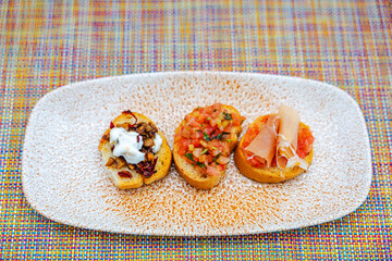 Close-up view of three bruschetta appetizers on textured plate with colorful woven tablecloth background. Mexico.