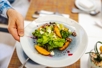 Close-up view of fresh salad with green lettuce, peach slices, nuts and cheese served on white plate with sauce drizzle. Mexico.