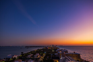 Scenic view of the Caribbean Sea coastline at sunset with vibrant orange and purple sky over illuminated hotels and calm water. Mexico. Cancun.