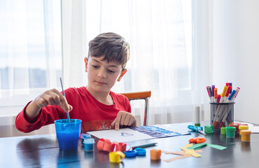 A boy draws at a table filled with colorful art supplies, themes of creativity, self-expression and...