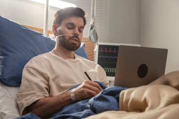 Hospitalized man working remotely on laptop with nasal cannula