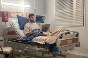 Young patient working on laptop while recovering in hospital bed