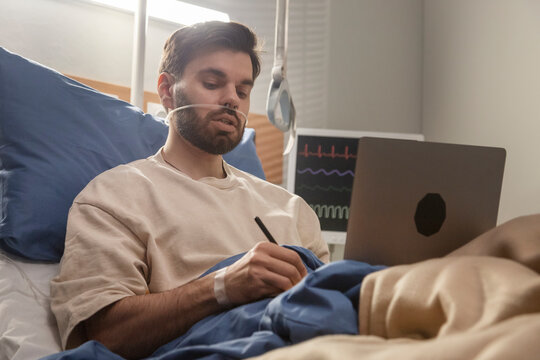 Hospitalized man working remotely on laptop with nasal cannula