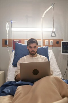 Young hospitalized patient working on laptop in modern hospital room