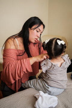 Mother dressing her baby daughter on bed in bedroom