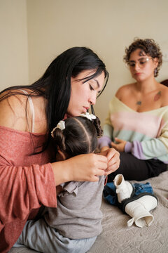 Lgbt mothers dressing their daughter on bed at home