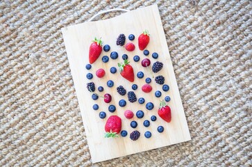 Different types of berries placed on a wooden cutting board, resting on a textured woven surface in natural light.