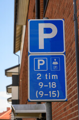 A blue parking sign indicates restrictions for two-hour parking between 9 AM and 6 PM on weekdays. The sign is mounted on a pole near a residential building