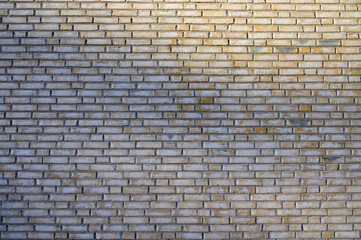 A weathered brick wall displays a uniform pattern with subtle variations in color. The soft natural light highlights the textures and imperfections, creating a serene atmosphere