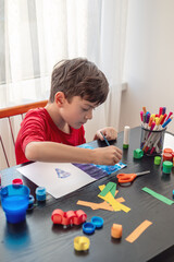 A boy draws at a table filled with colorful art supplies, themes of creativity, self-expression and...