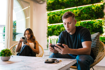 Friends using smartphones in modern cafeteria with vertical garden