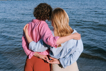 Two women stand on the beach beside the ocean, enjoying a sunny day