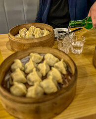 Asian dumplings in a wooden bowl on a wooden table with a bottle with soju on the background