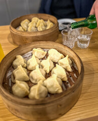 Asian dumplings in a wooden bowl on a wooden table with a bottle with soju on the background