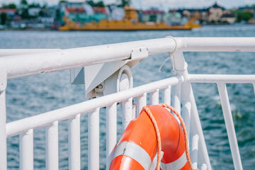 Orange lifebuoy hanging on white railing of ferry boat with cityscape in background