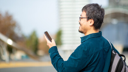 Asian man using smartphone outdoors with an urban background