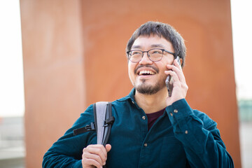 Asian man smiling and looking up while holding a smartphone