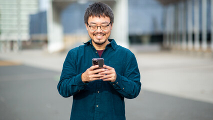 Smiling Asiatic man using a smartphone in an urban outdoor setting