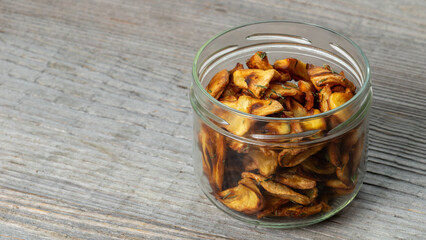 Parsnip chips in a glass jar. Rustic wooden background with space for text.