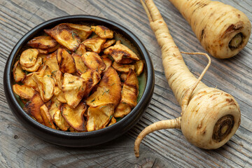 Parsnip chips with honey and thyme in a bowl.  On the side raw parsnip roots.