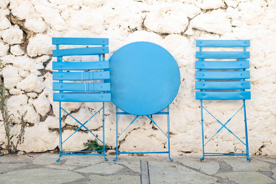 Folded cafe table and two chairs against white wall in Greece