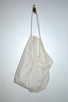 A simple white canvas bag hanging on a hook against a plain wall 