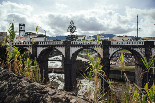 Historic stone bridge with arches near a town under cloudy sky