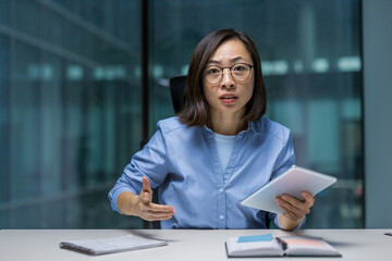 Angry and irritated woman looking at camera, businesswoman chatting with colleagues at online business meeting, webcam view. Asian office worker at workplace.