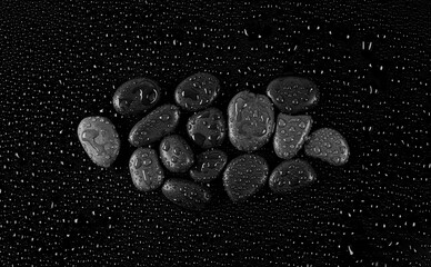 Oval stones with water drops on black background, top view	