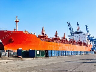 Fototapeta premium Container ship docked at a busy port with clear skies and cranes in the background