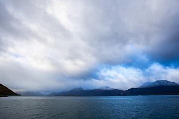 Autumn landscape of the Lyngen Alps in Northern Norway with snowy peaks, dramatic clouds, and a tranquil fjord.