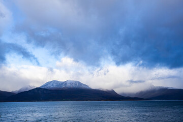Autumn landscape of the Lyngen Alps in Northern Norway with snowy peaks, dramatic clouds, and a tranquil fjord.