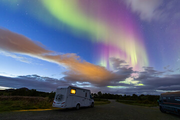 A motorhome parked under the stunning Northern Lights in Lofoten Islands, Norway, with colorful auroras in the sky.