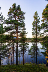 A peaceful sunset over a lake in Lapland, Sweden, with the reflection of trees in the still water.