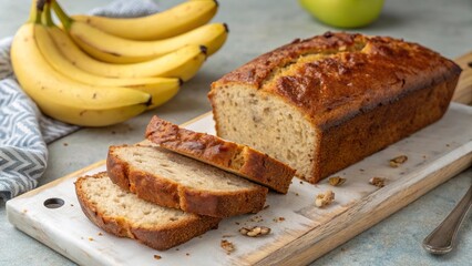 Freshly baked banana bread loaf with sliced pieces on a wooden board surrounded by ripe bananas