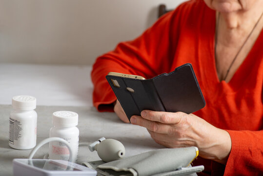 Faceless mature woman watching smartphone at the table with medicines