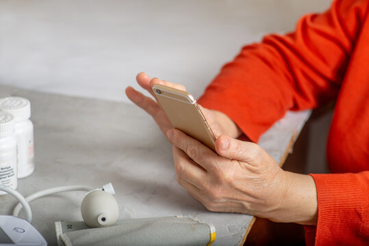 Faceless mature woman scrolls smartphone at the table with medicines