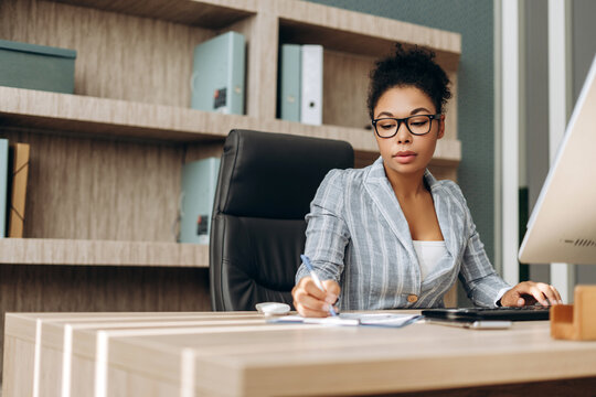 Serious businesswoman working on computer and taking notes in modern office