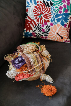 A basket of yarn standing on the sofa next to the cushion