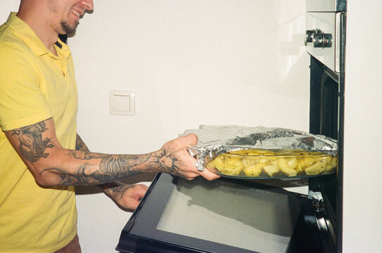 A smiling man puts a tray with potatoes in the oven 
