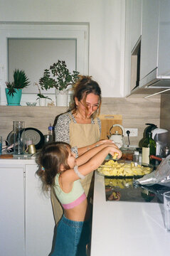 A young mom teaches her young daughter how to cook in the kitchen