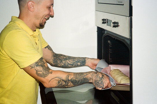 A smiling man puts a tray of apple pie in the oven 