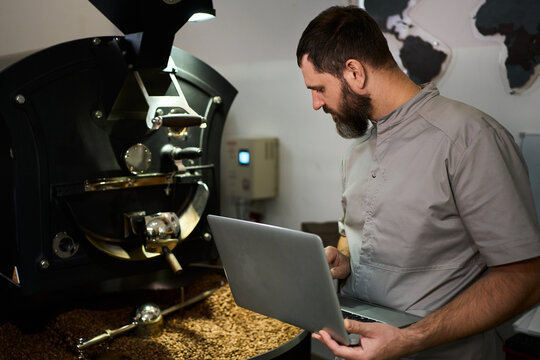 Barista roasting coffee beans in a workshop while using a laptop